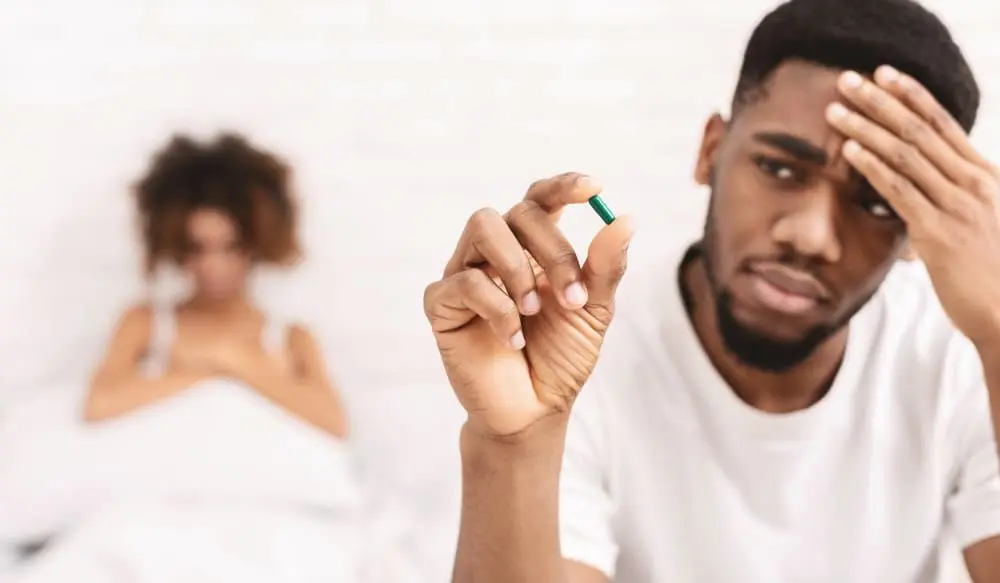 Concerned man holding a pill with a woman in the background