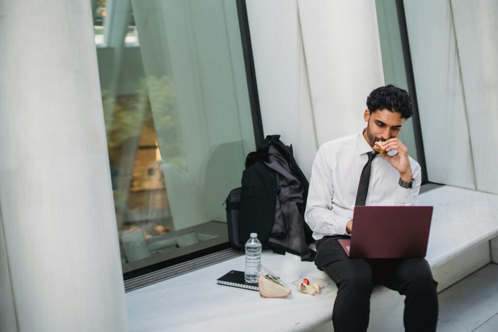 pexels-photo-4964978-4964978 Businessman in formal attire eating lunch and working on a laptop outside an office building.