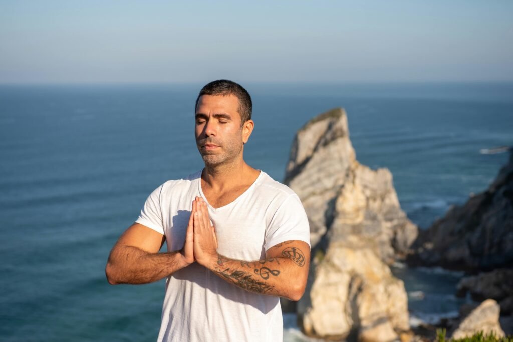 Men's Health Men's Health practicing meditation by the sea with a rocky backdrop in Portugal, capturing serenity and focus.