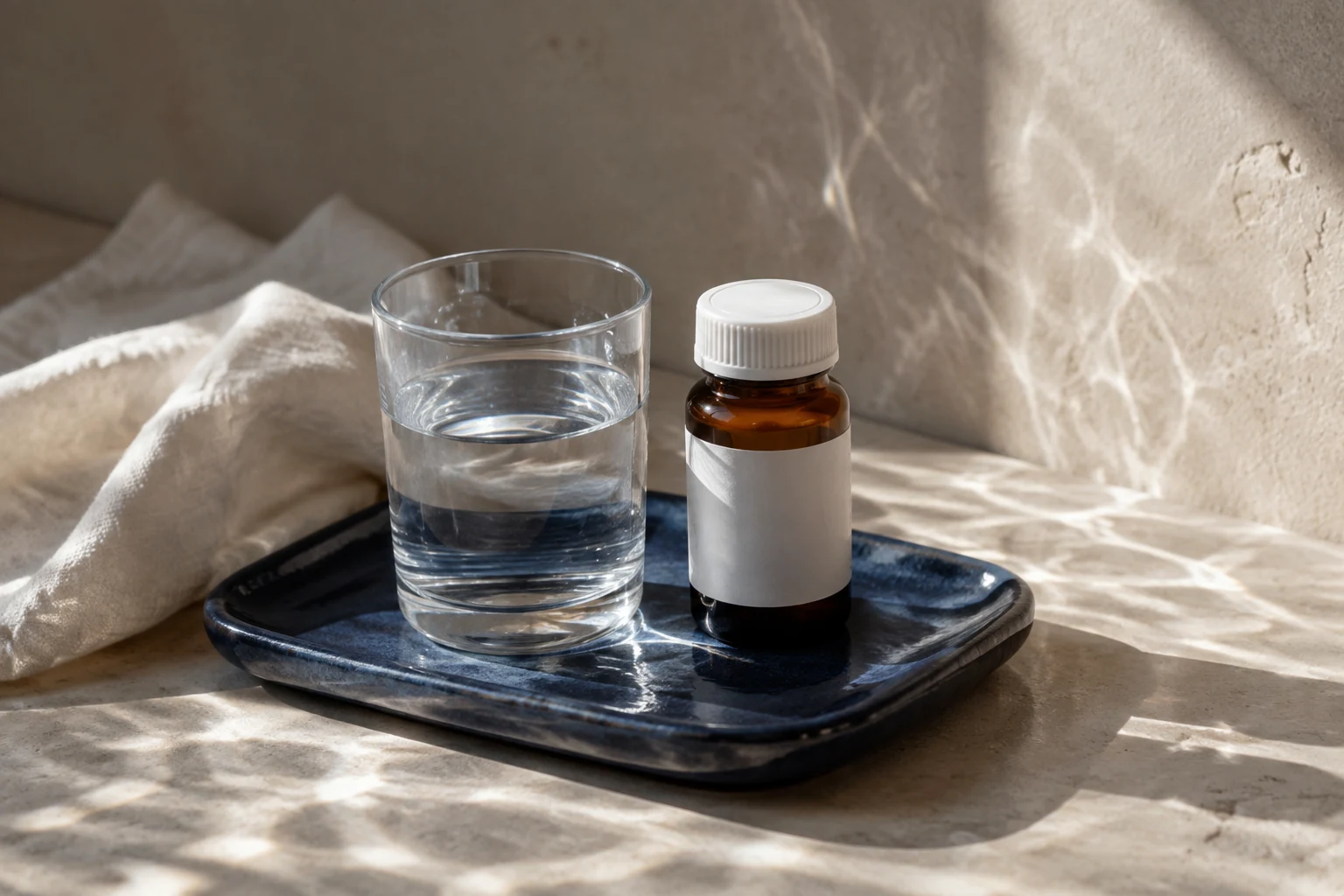 Glass of water and an unbranded closed medicine bottle on a cobalt ceramic tray