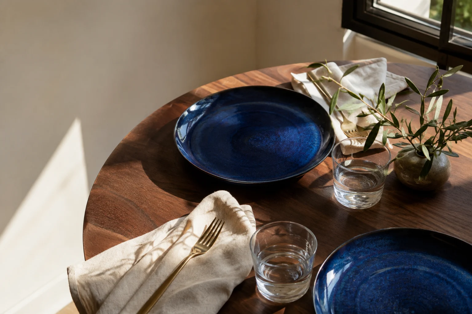 Two cobalt-blue place settings on a sunlit wooden table beside a window
