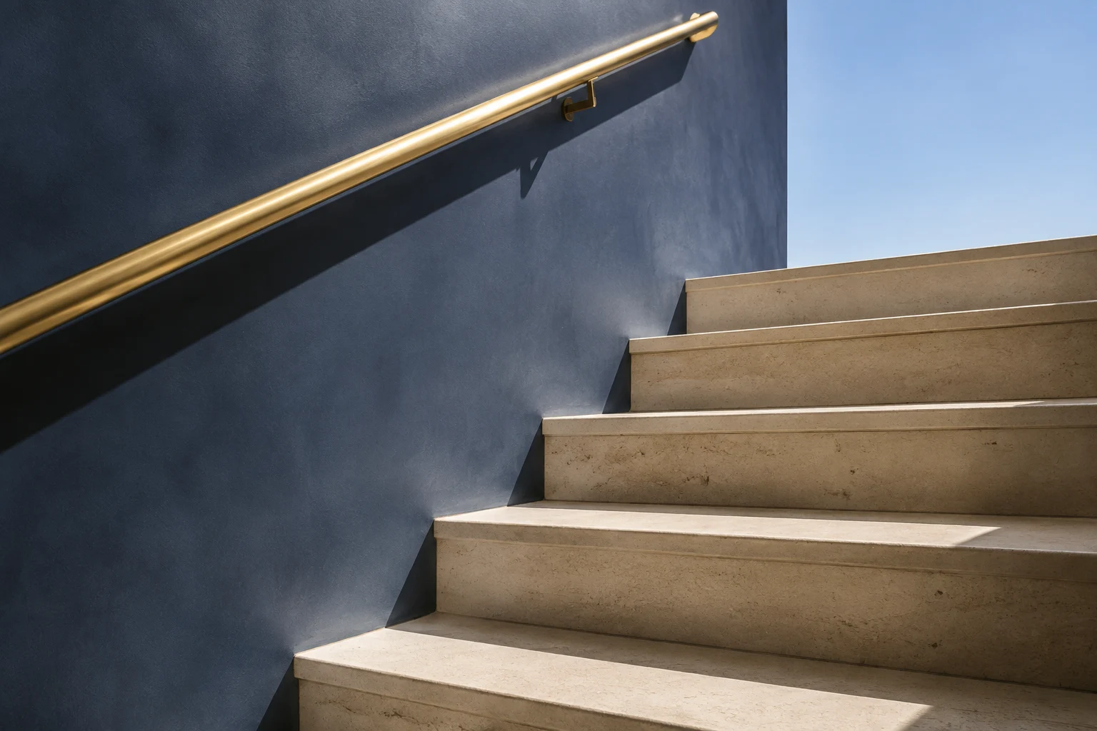 Sunlit limestone steps beside a slate-blue wall and brass handrail