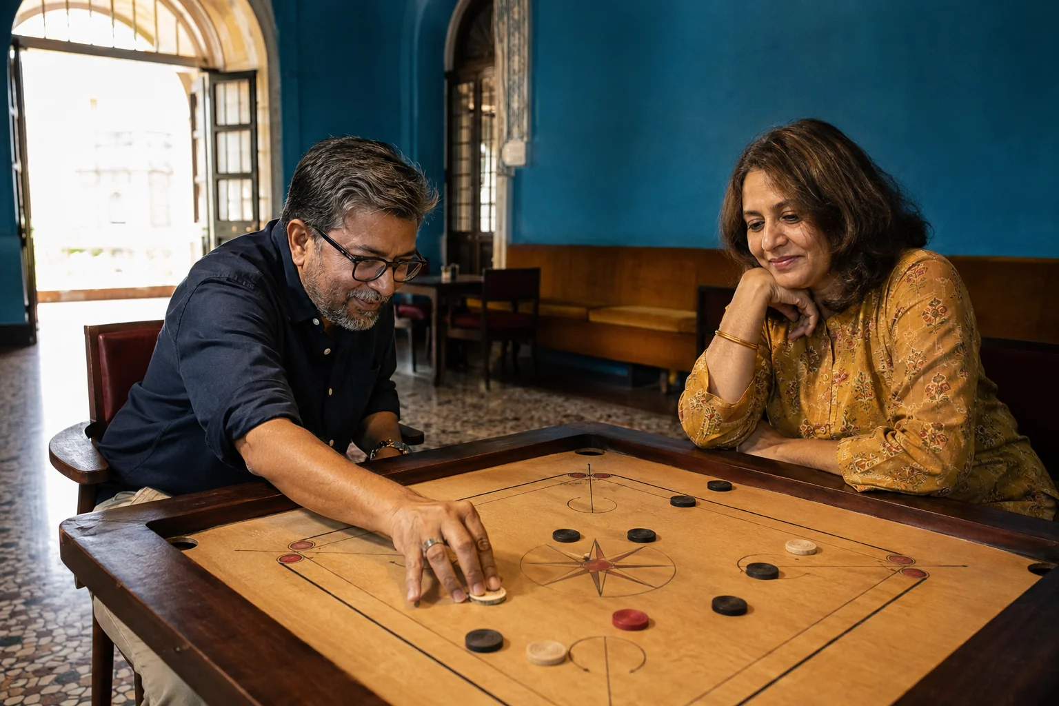 A couple sharing a relaxed game of carrom in a blue-walled social club