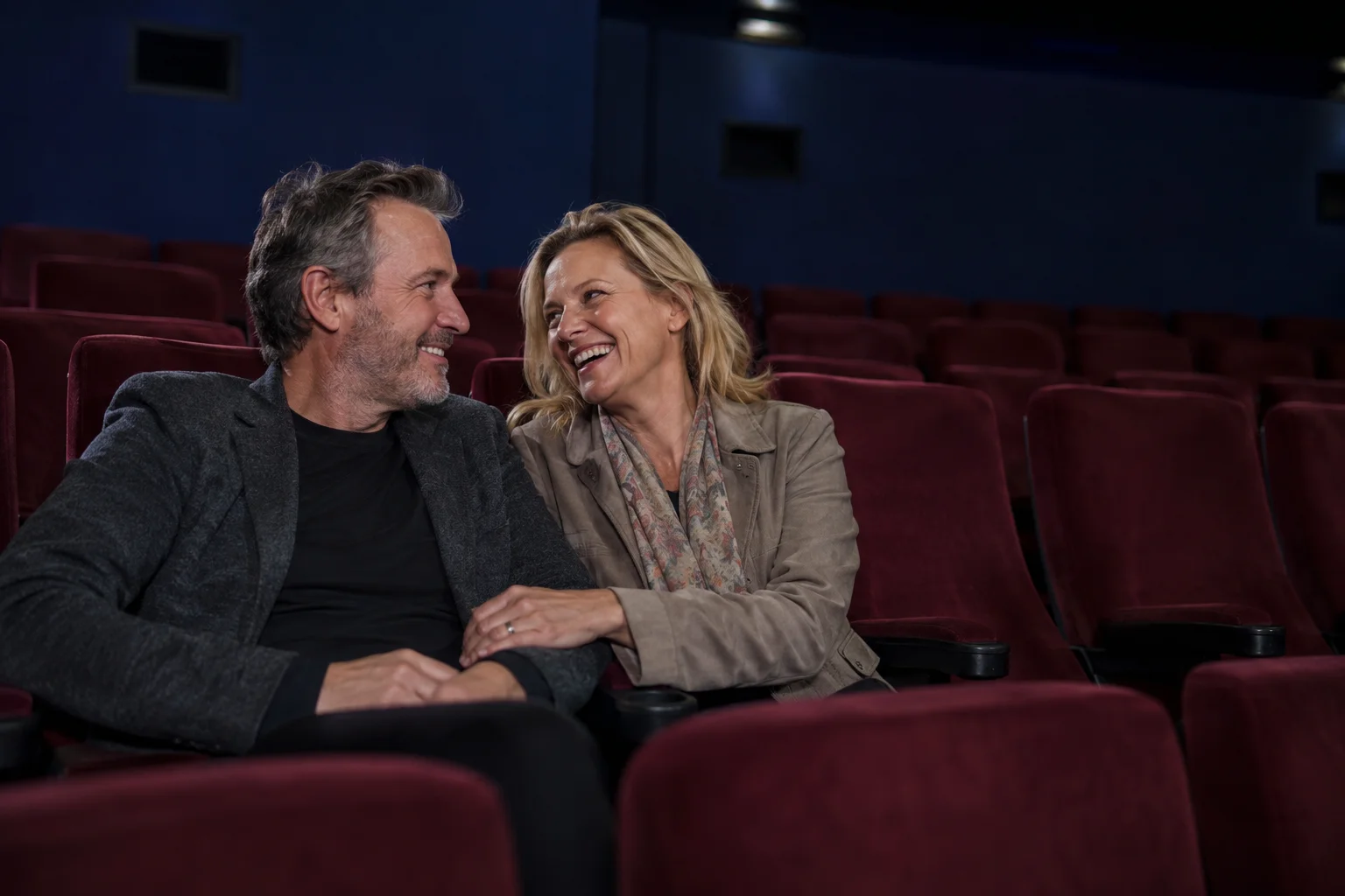 A mature couple sharing a quiet laugh in a small cinema before the film begins