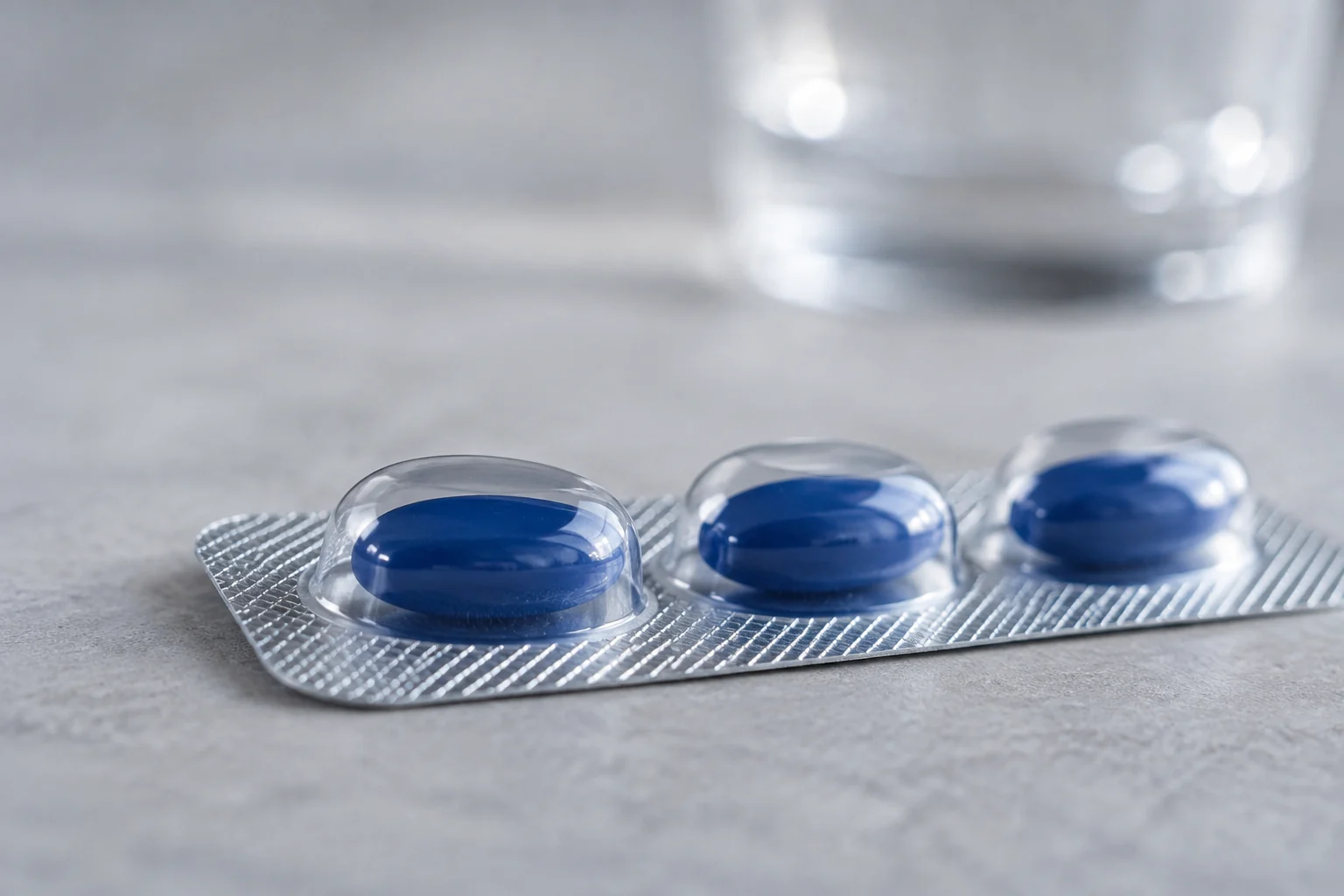 Macro photograph of blue oval softgel capsules sealed in a silver blister