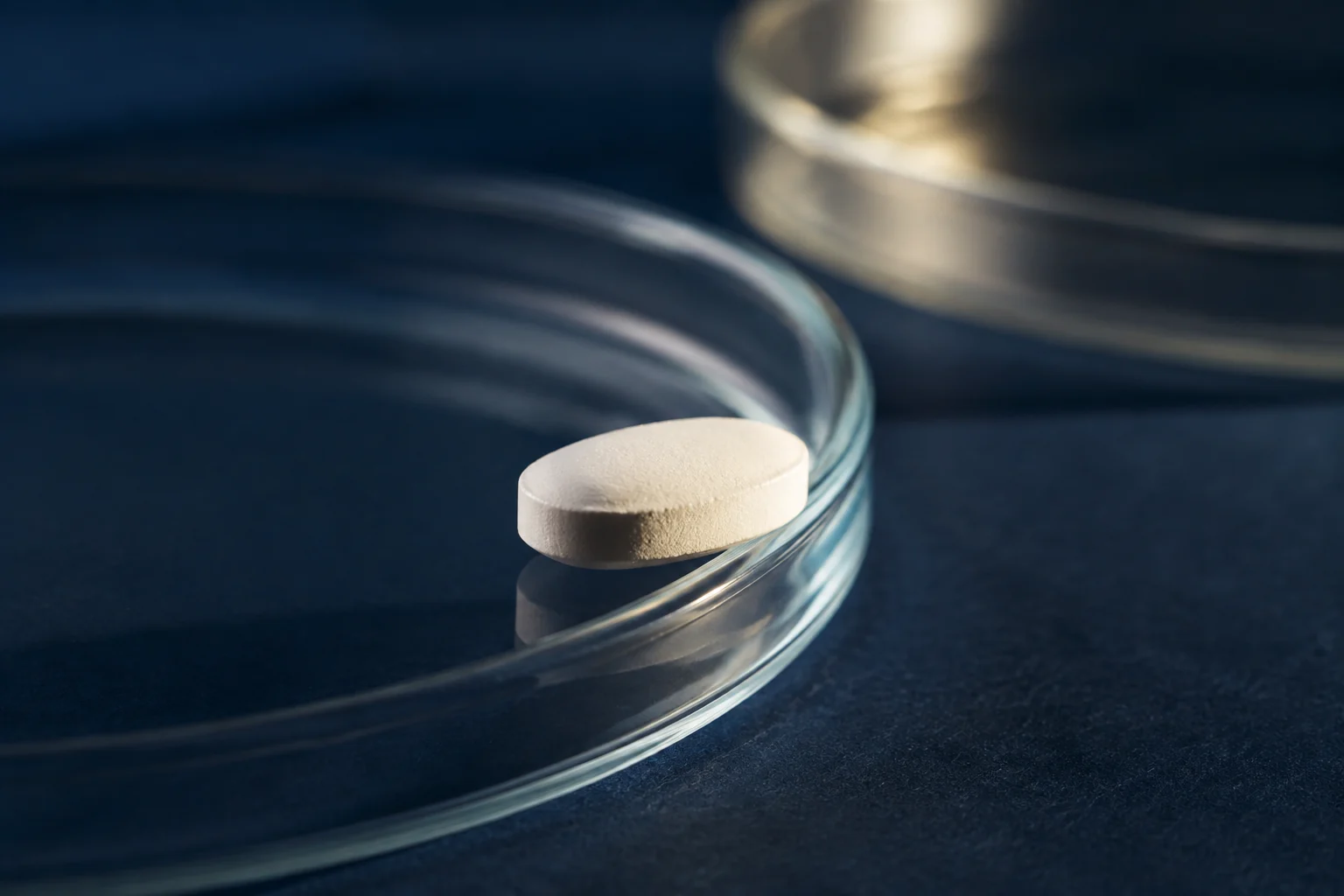 Macro view of an unmarked white tablet beside the rim of a clear glass dish.