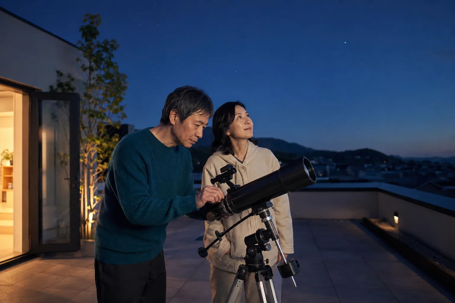 Two adults setting up a telescope on a rooftop terrace at dusk.