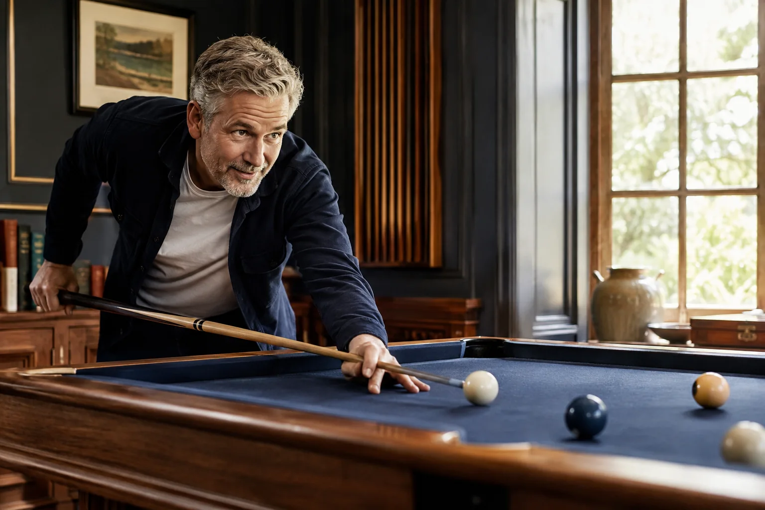 A mature man lining up a shot at a blue billiards table in a sunlit room