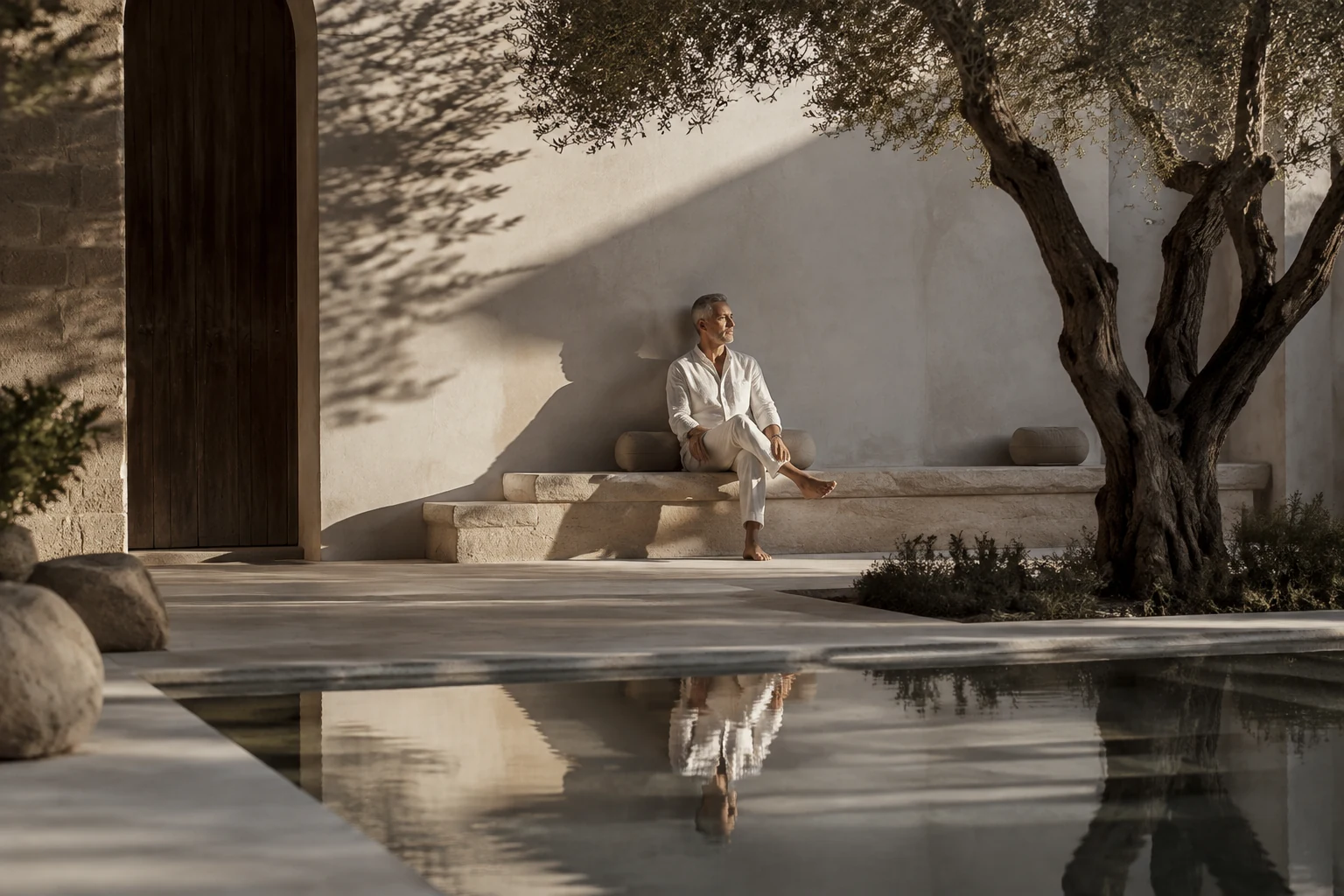 Man resting in a secluded olive-tree courtyard beside a reflecting pool