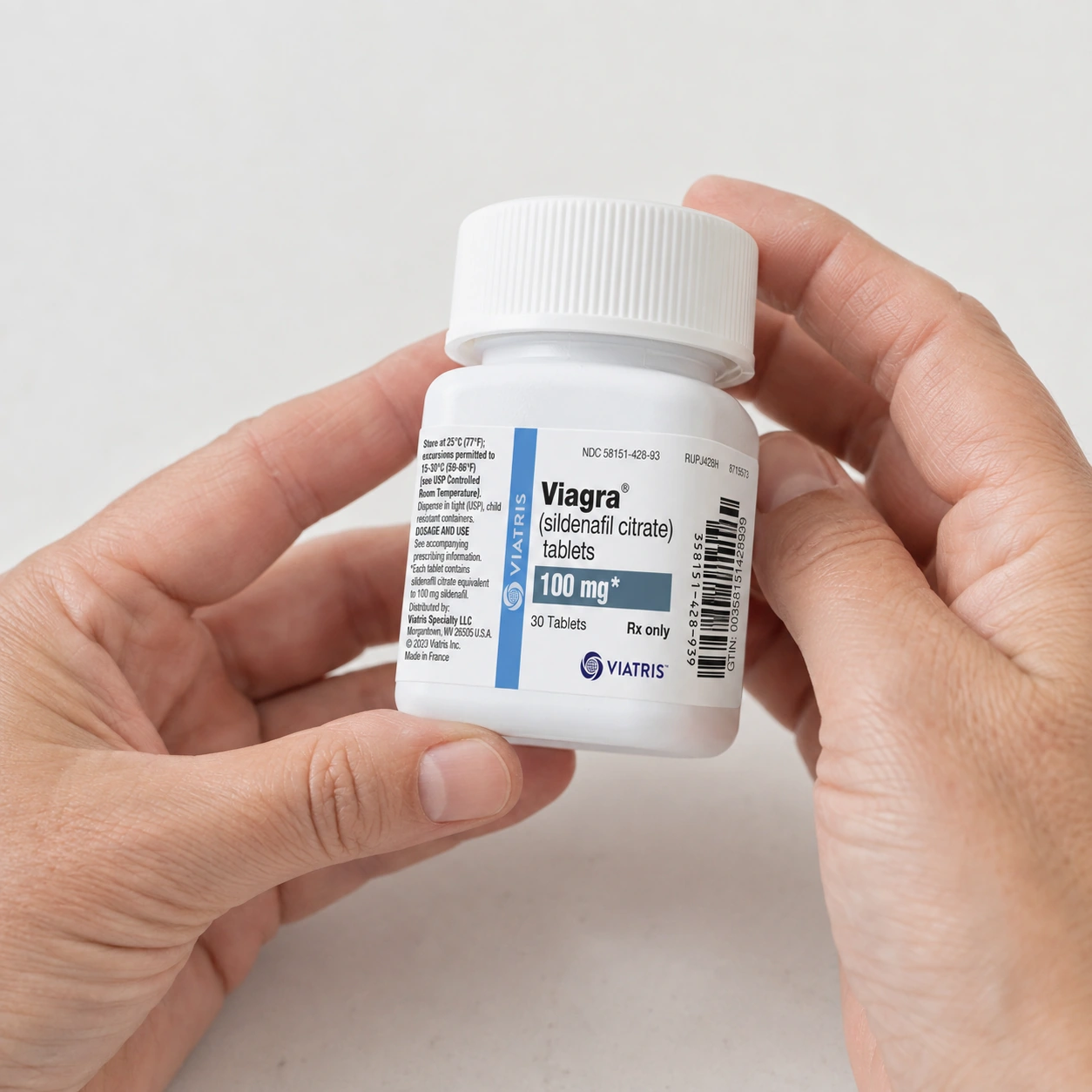 Illustration of hands holding a closed Viagra 100 mg bottle to read its label above a clean white desk.