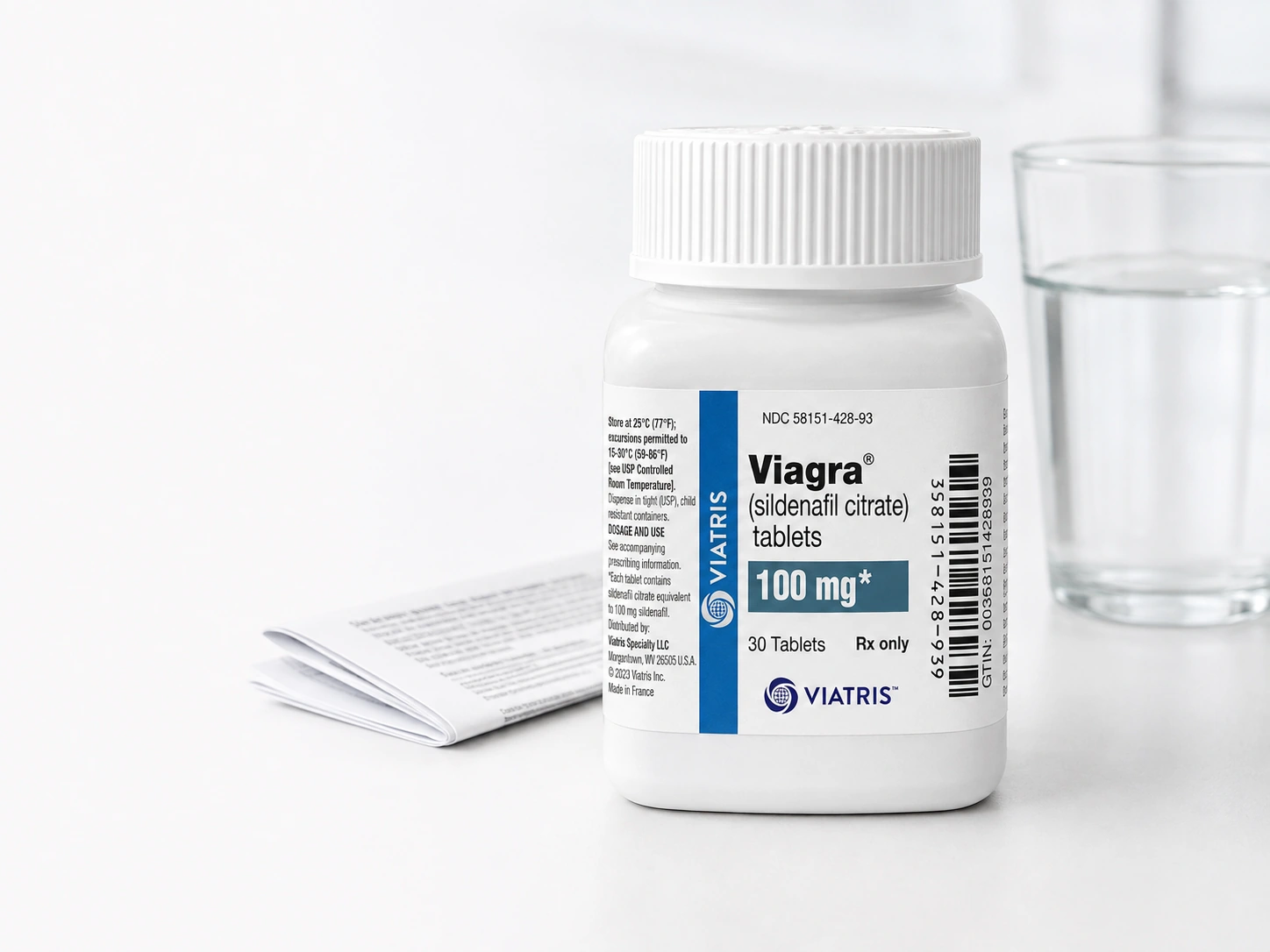 Illustration of a Viagra 100 mg bottle standing beside a folded medicine leaflet and a glass of water on a white desk.